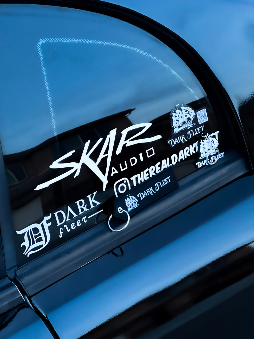 Car window with multiple stickers including 'SKAR Audio' and 'Dark Fleet'.