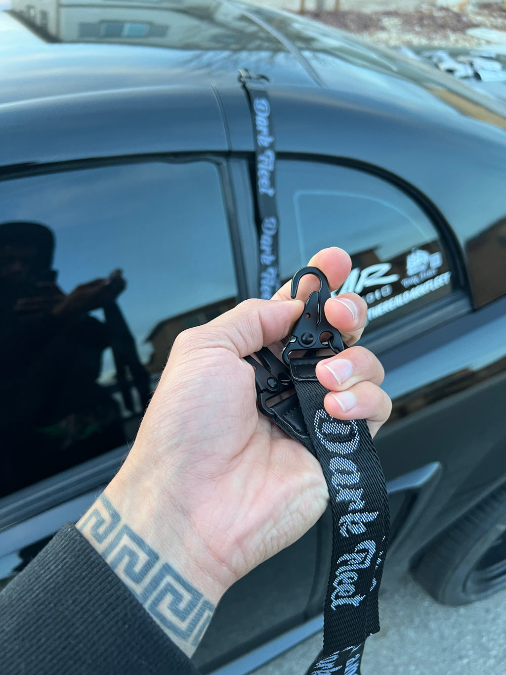 Hand holding a black lanyard with 'Dark Fleet' branding in front of a car.