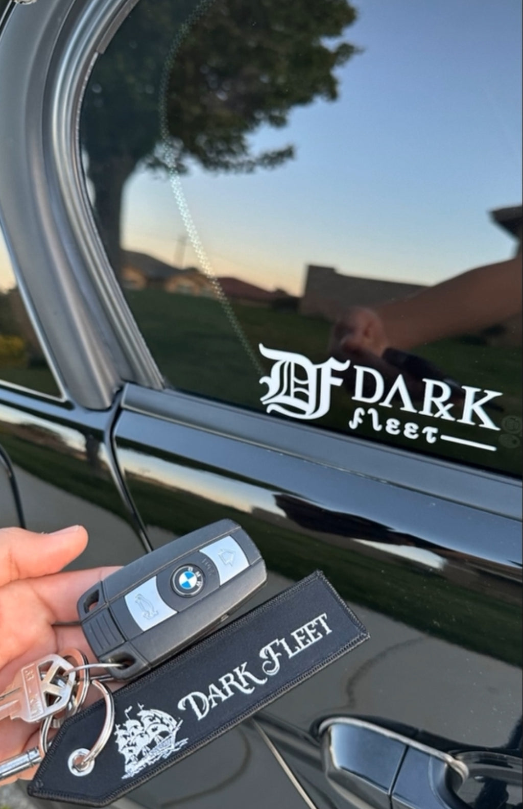 Car window with 'Dark Fleet' decal, key fob, and keys held by a hand.