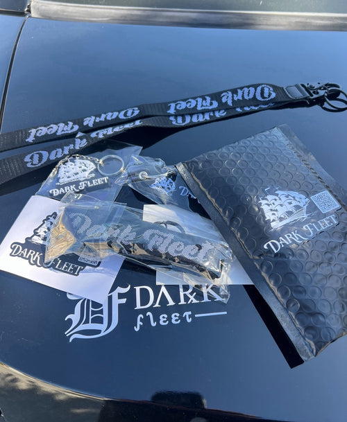 Dark Fleet merchandise including a lanyard, stickers, and a bubble-wrapped item on a car hood.